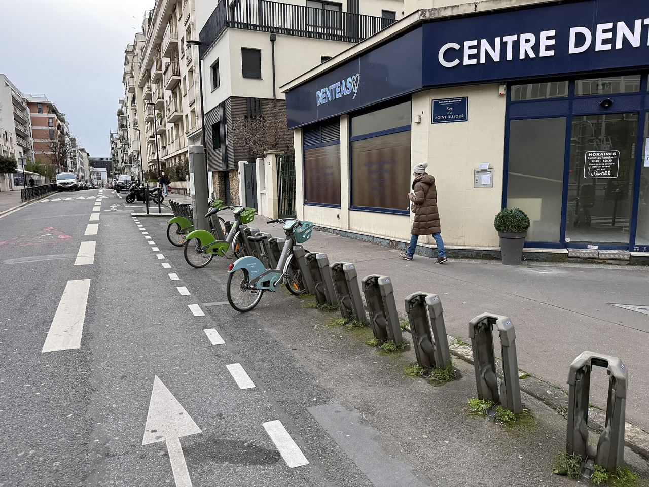 Station Vélib' Point du Jour – Jean Jaurès à Boulogne-Billancourt : une rangée de vélos verts et bleus à leurs bornes, le long d'une rue marquée de flèches au sol.