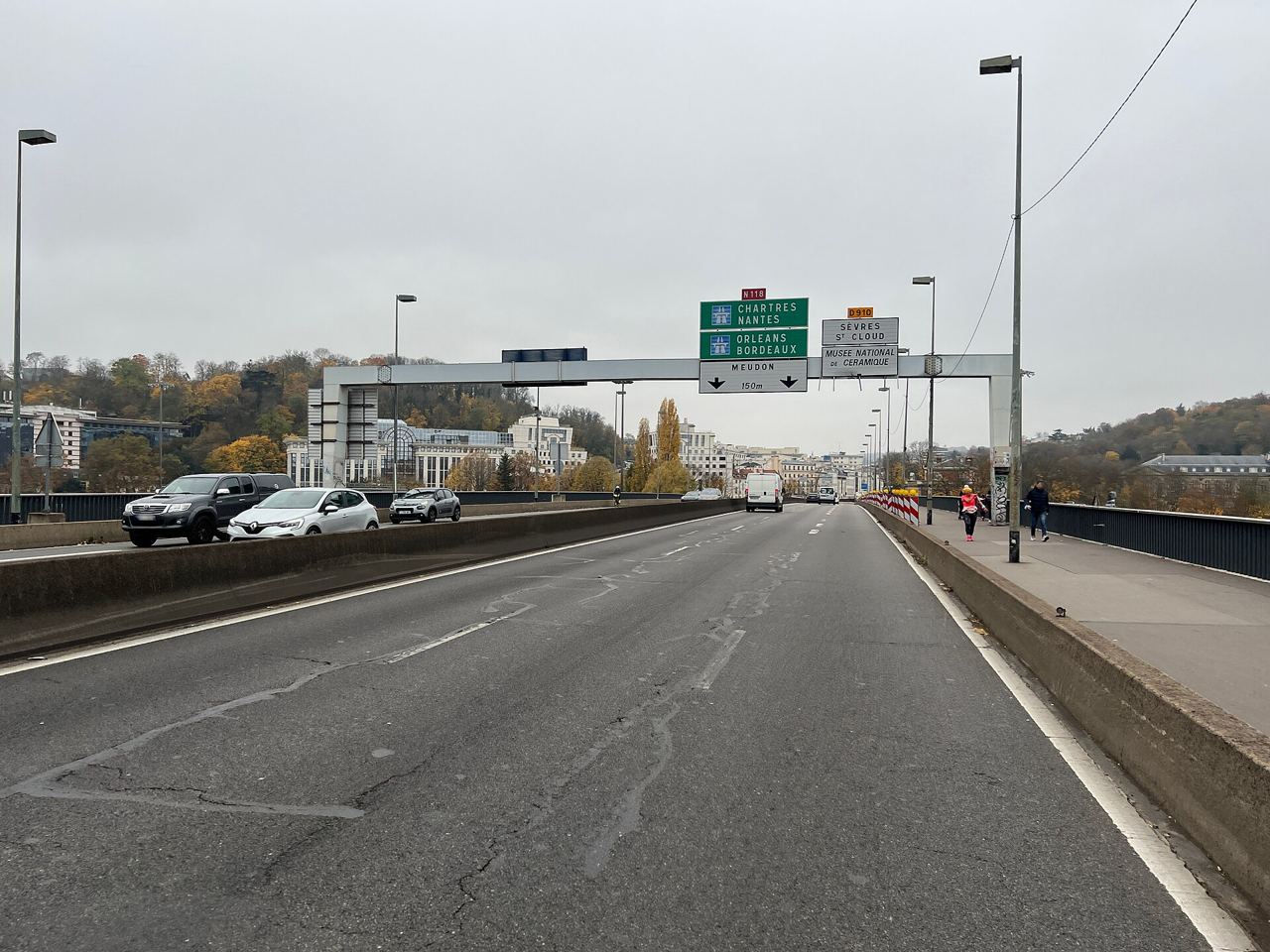 Le pont de Sèvres vu depuis Boulogne-Billancourt : quatre voies de circulation sous les portiques de signalisation, un trottoir étroit à droite et les coteaux boisés de Sèvres au fond.